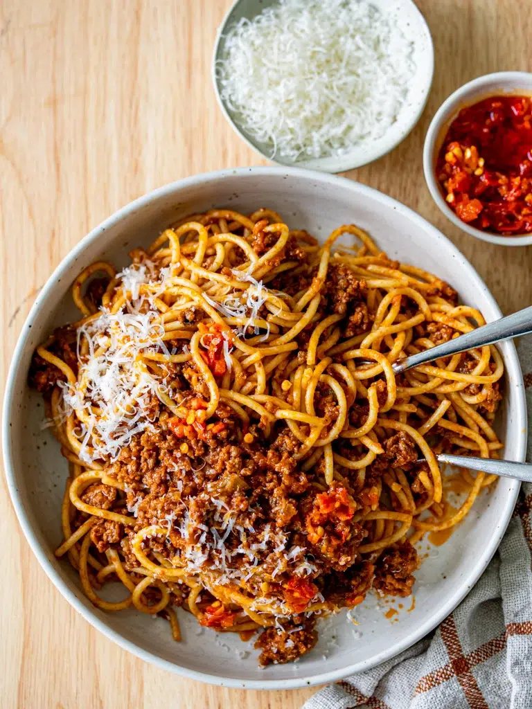 Top view of Bolognese sauce served with cutlery and red chilli on the side.