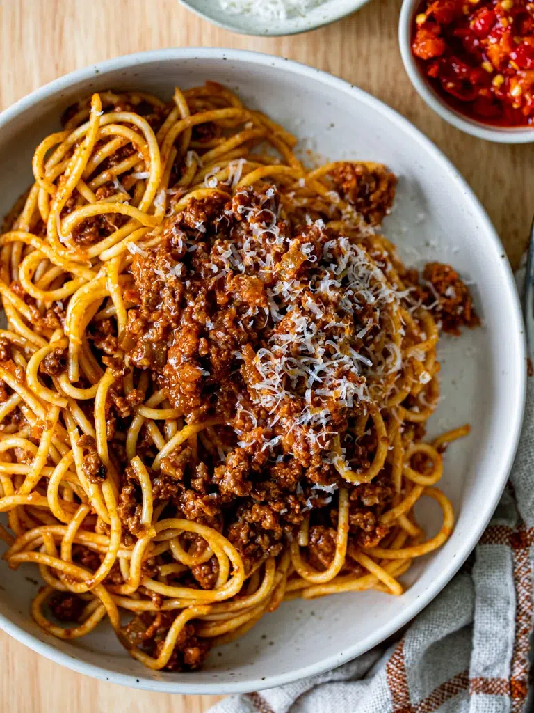 Top view close-up of freshly made Bolognese sauce served in a white bowl with pasta.