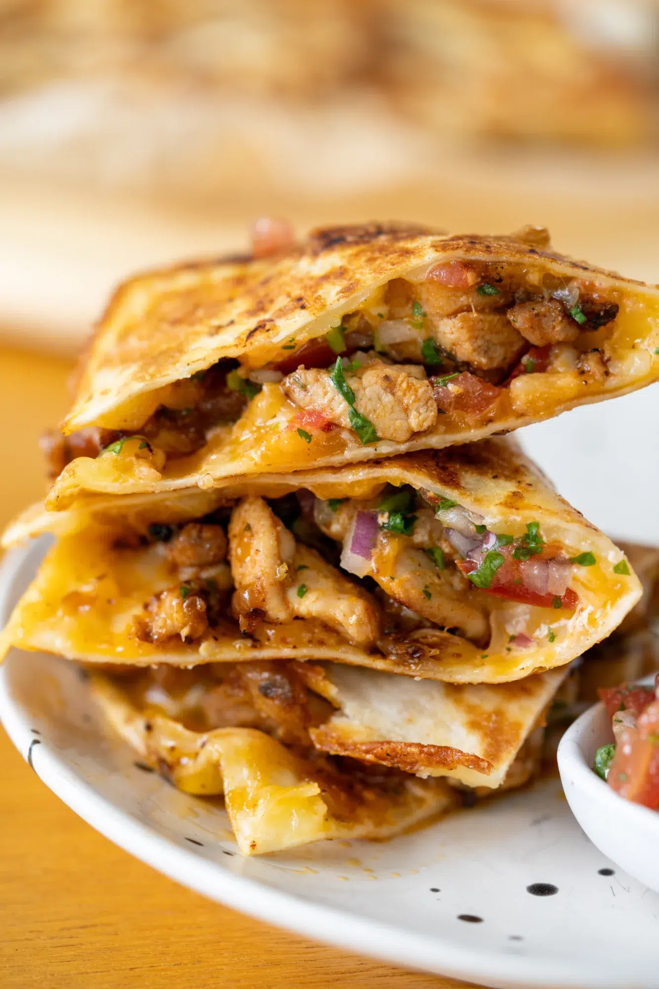 Close-up of cheesy chicken quesadillas stacked on a plate, filled with seasoned chicken, pico de gallo, and melted cheese