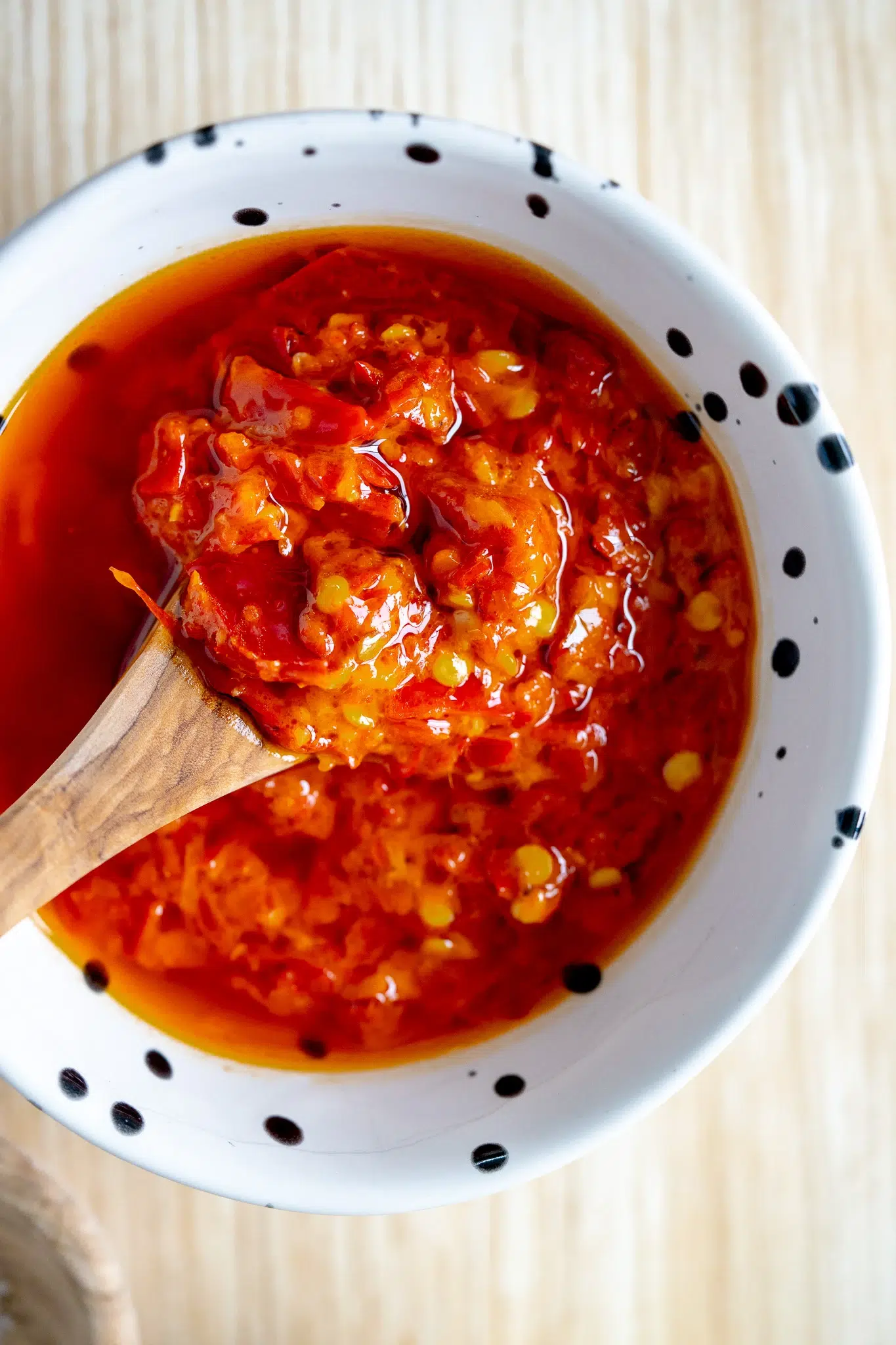 Close-up of Portuguese-style chili sauce in a small bowl with a wooden spoon dipped in