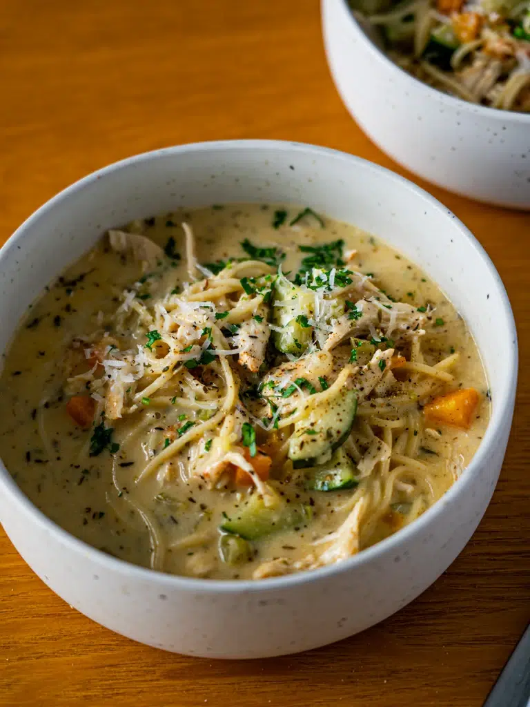 Sideways view of two bowls of creamy lemon chicken noodle soup.