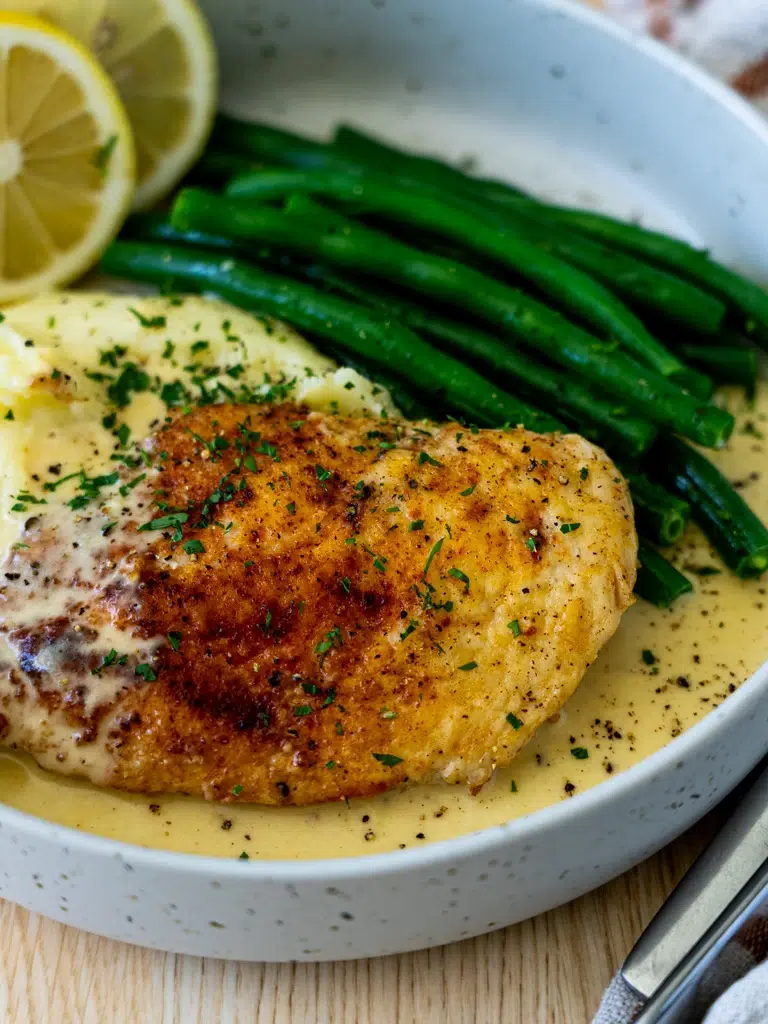 Side view of a plated Creamy Lemon Pepper Chicken with green beans, mashed potatoes, and a rich sauce.