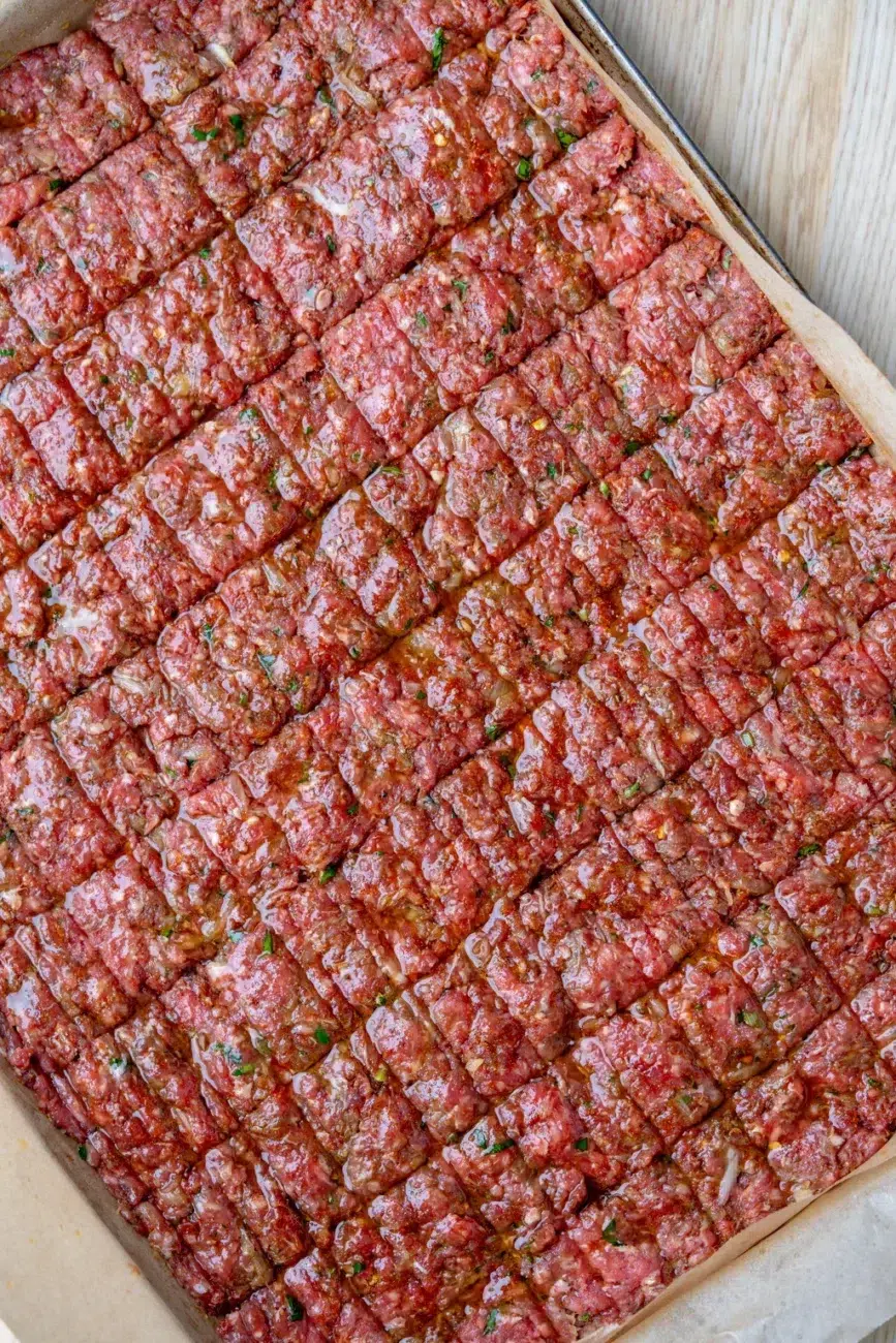 Spiced ground meat mixture scored into kebab portions in a baking tray, brushed with oil and ready for oven baking