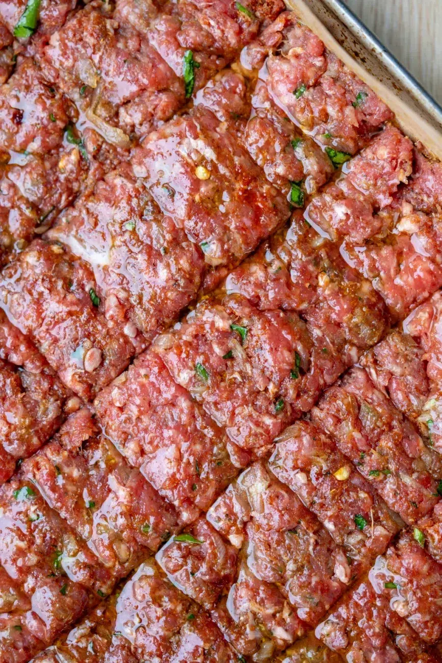 Close-up of scored and oiled spiced ground meat mixture in a baking tray, prepared for oven-baked kebabs