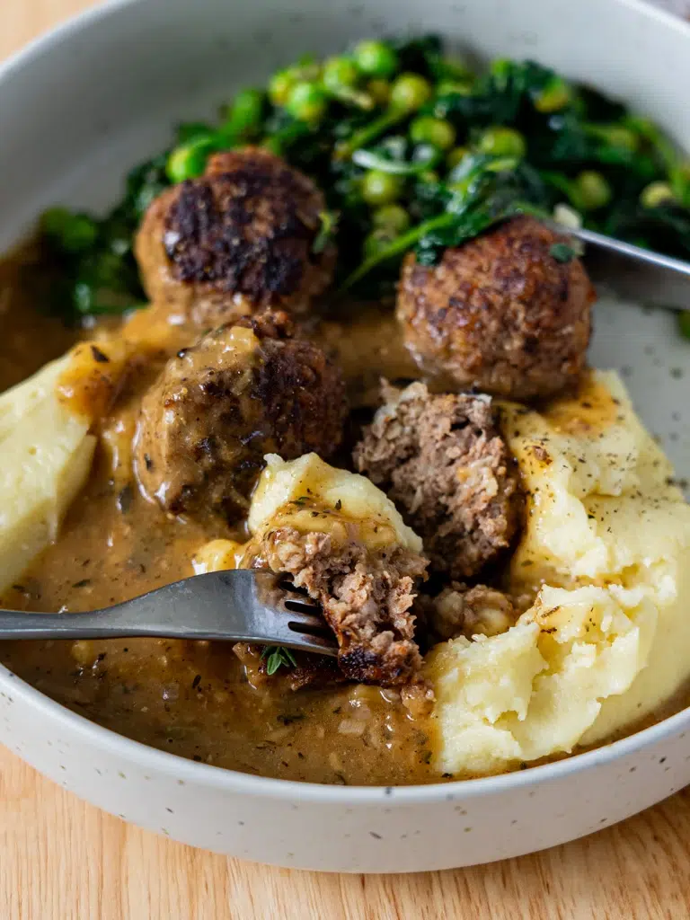 Juicy meatballs covered in rich, silky gravy, served on a plate.