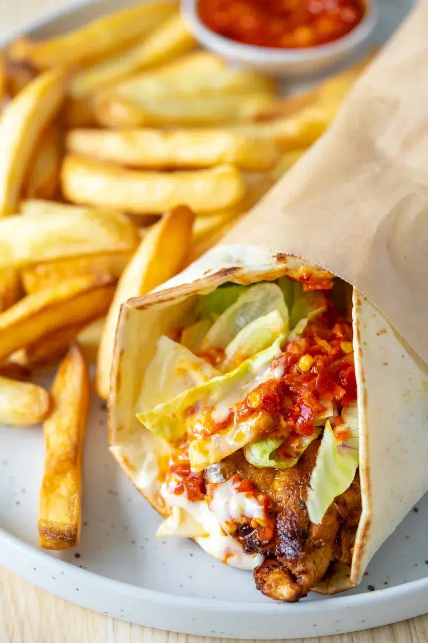 lose-up of Portuguese-style chili chicken wrap with lettuce, sauce, and fries on a plate
