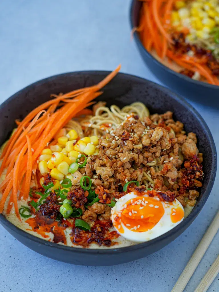 Bowl of ramen noodles with ground meat, corn, carrots, and soft-boiled egg