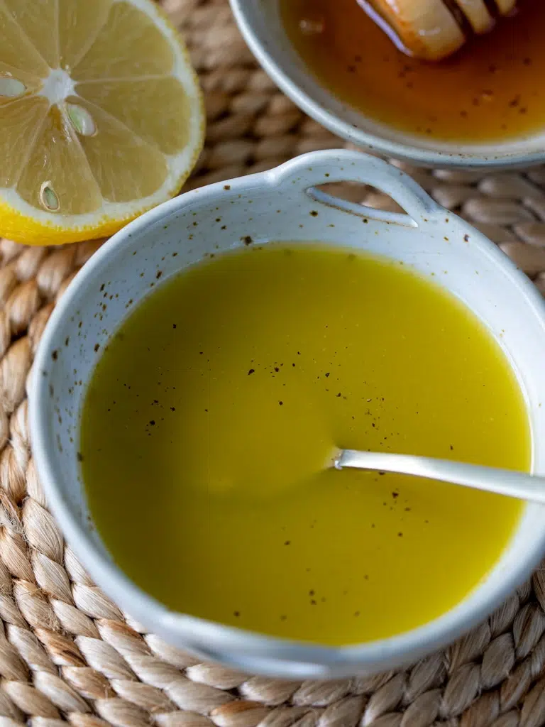 Homemade salad dressing made with olive oil, black pepper, and lemon, served in a ceramic bowl with a spoon.