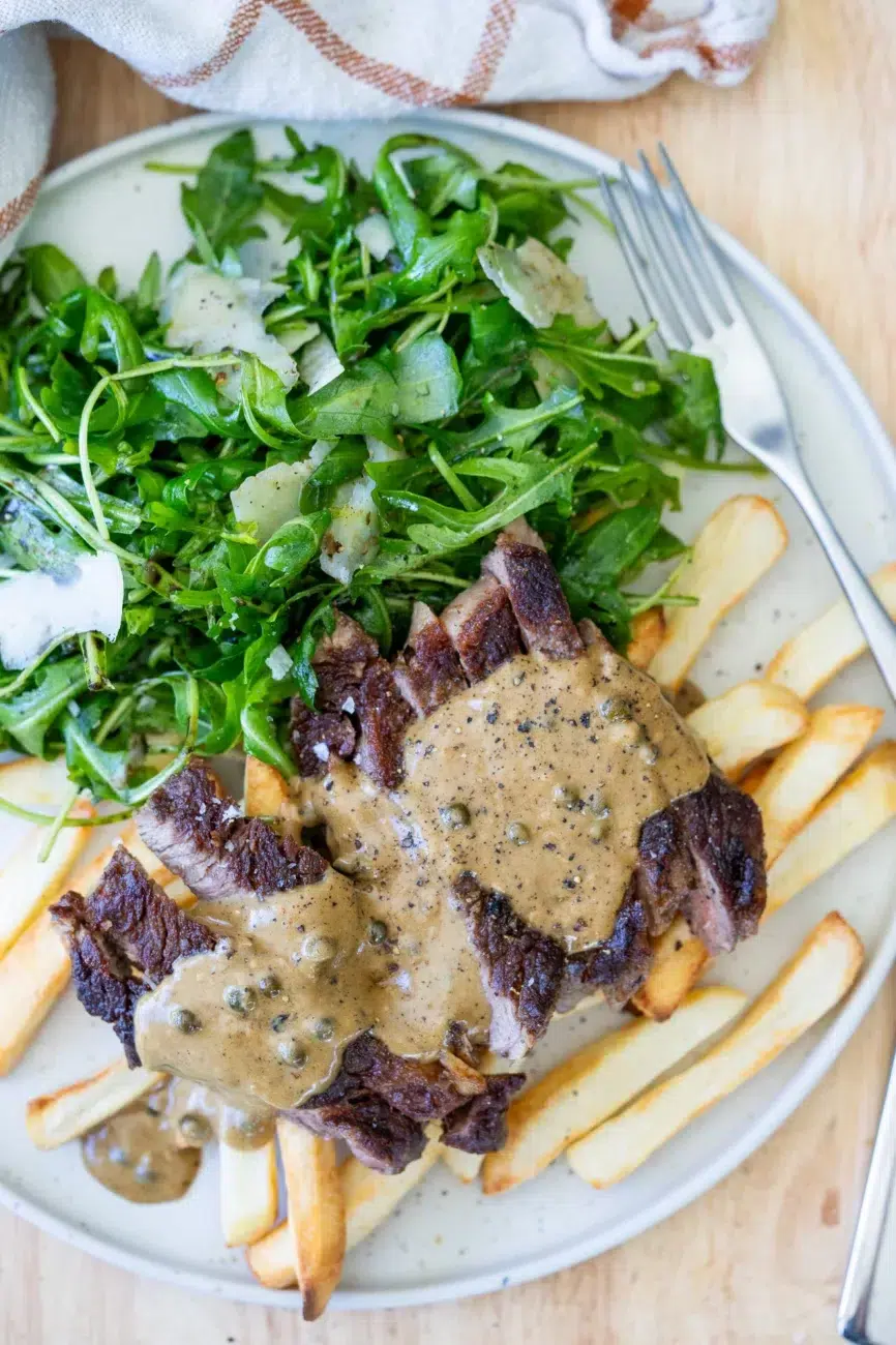 Steak with peppercorn sauce recipe served over fries and arugula salad